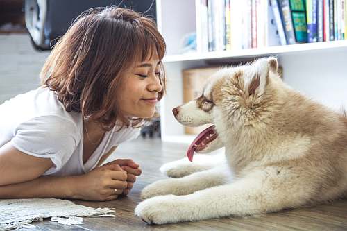 Woman lying on the floor face-to-face with a light-colored husky dog